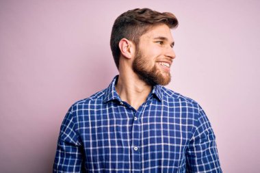 Sakallı, mavi gözlü, sıradan gömlekli, yüzünde gülümsemeyle yan yana duran yakışıklı sarışın bir adam. Kendinden emin gülen.