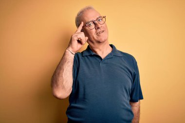 Orta yaşlı, yakışıklı, beyaz tenli, polo giyen, sarı arka planda gözlüklü, tek parmakla başını gösteren, harika bir fikir ya da düşünce, iyi bir hafıza.