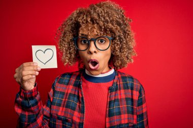 Genç Afro-Amerikan kıvırcık kadın elinde kırmızı arka planda kalbi olan hatırlatma kâğıdı tutuyordu. Şaşırmış bir yüzle korkmuş ve korku ifadesinden korkmuştu.