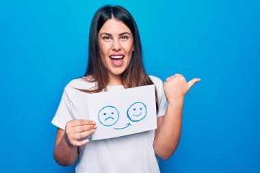 Kadın psikoloji değişikliği istiyor. Elinde mutsuz ve mutlu bir duygu mesajı olan kâğıtlar var. Başparmağını kaldırıp gülümsüyor ve ağzını açıyor.
