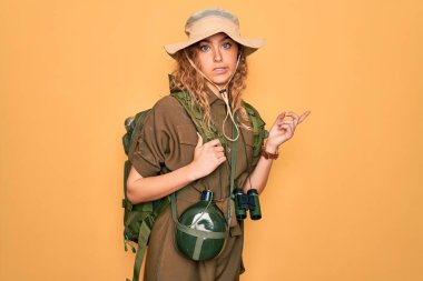 Mavi gözlü genç sarışın kaşif sırt çantası ve su matarası takıyor. Endişeli ve endişeli bir ifade takınıyor.