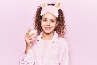 Kıvırcık saçlı, uyku maskesi takan güzel bir kız ve elinde süt tutan bir pijama. Pozitif ve mutlu görünüyor. 