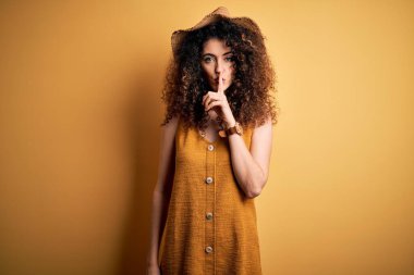 Güzel esmer kadın tatilde, kıvırcık saçlı, piercingli, şapkalı ve elbiseli dudakları parmaklı sessiz olmak istiyor. Sessizlik ve gizli konsept.