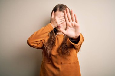 Genç, güzel, kızıl saçlı bir kadın, izole edilmiş beyaz arka plan üzerine günlük süveter giyer, gözleri ellerle kapatır ve üzgün ve korku ifadeleriyle dur hareketi yapar. Utanç verici ve olumsuz bir kavram..