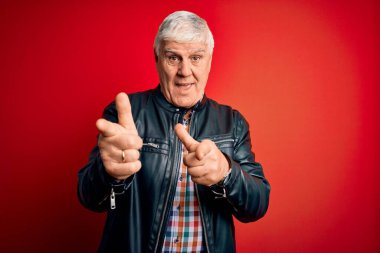 Kıdemli yakışıklı, beyaz gömlekli ve ceketli adam izole edilmiş kırmızı arka plan üzerinde mutlu ve komik yüzlü parmakları kameraya gösteriyor. İyi enerji ve titreşimler.