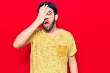 Gündelik kıyafetler giyen genç İspanyol adam şok içinde yüzünü ve gözlerini eliyle kapatıyor, parmaklarından korkuyla bakıyor. 