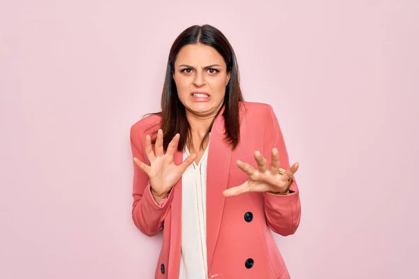 Young beautiful brunette businesswoman wearing elegant jacket over isolated pink background disgusted expression, displeased and fearful doing disgust face because aversion reaction.