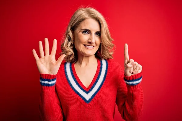 Middle age beautiful blonde woman wearing casual sweater over isolated red background showing and pointing up with fingers number six while smiling confident and happy.