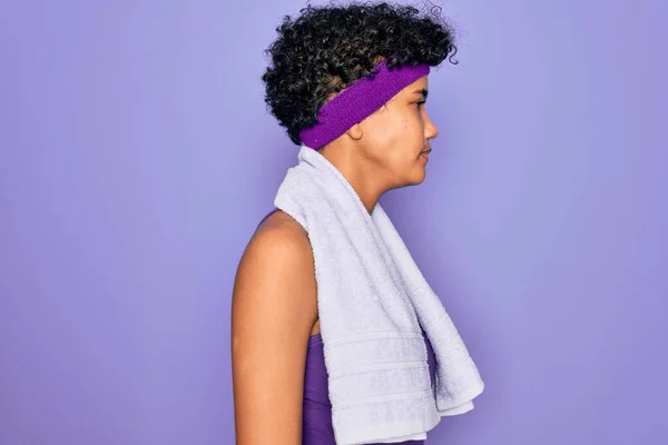 美しいアフリカ系アメリカ人のスポーティな女性は サイドを見て紫色の背景にタオルを身に着けているスポーツをやって 自信を持って笑顔で自然な顔でプロファイルポーズをリラックス — ストック写真