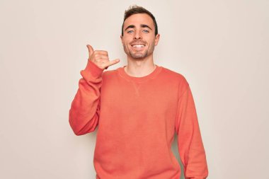 Mavi gözlü, sıradan bir süveter giyen, beyaz arka plan üzerinde gülümseyen, el ve parmaklarıyla telefonla konuşan genç yakışıklı bir adam. İletişim kavramları.