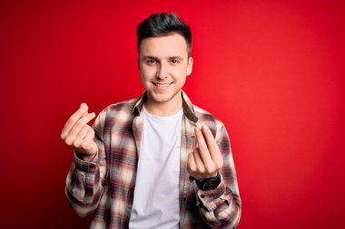 Genç, beyaz, gündelik modern gömlek giyen, kırmızı izole edilmiş arka planda para hareketi yapan, maaş ödemesi isteyen, milyonerlik işi yapan yakışıklı bir adam.