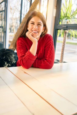 Genç ve güzel esmer kadın mutlu ve kendinden emin gülümsüyor. Yüzünde gülümsemeyle oturup restoranda rahatlamak.