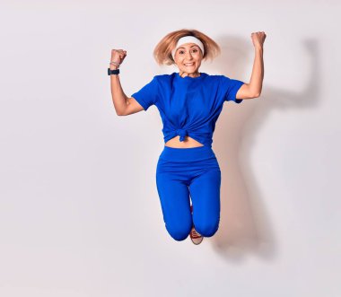 Genç beyaz kadın spor giyer, mutlu bir şekilde gülümser. Yüzünde tebessümle zıpla kazanan imzayı at yumruklarınla yalıtılmış beyaz arka planda