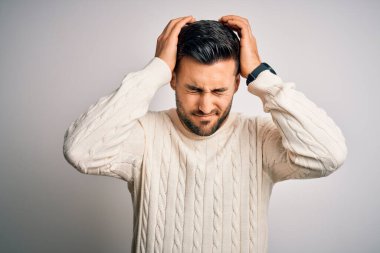 Young handsome man wearing casual sweater standing over isolated white background suffering from headache desperate and stressed because pain and migraine. Hands on head.