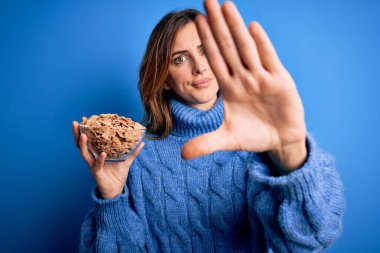 Genç, güzel esmer kadın elinde kaseyle sağlıklı mısır gevreği gevrekleri ve açık elle dur işareti yapıyor. Ciddi ve kendinden emin bir ifadeyle, savunma jesti.