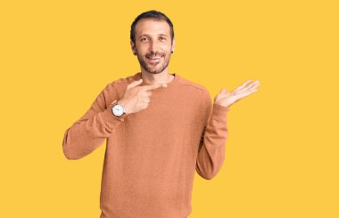 Gündelik kıyafetler giyen genç yakışıklı adam kameraya hayret ediyor ve gülümsüyor.. 