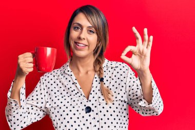 Bir fincan kahve içen genç güzel bir kadın parmaklarıyla imza atıyor, gülümseyerek mükemmel bir sembol oluşturuyor. 