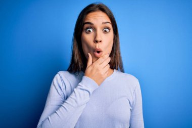 Mavi arka planda sıradan bir süveter giyen genç, güzel esmer kadın elleri çenesinde olan inançsızlıktan, şaşkınlıktan ve şaşkınlıktan büyülenmiş görünüyor.