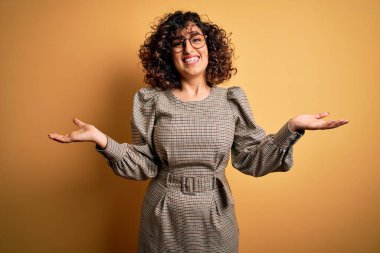 Güzel bir Arap iş kadını. Elbise ve gözlük takıyor. Sarı arka planda duruyor.