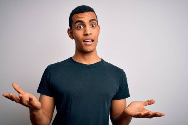 Genç, yakışıklı, Afro-Amerikalı bir adam beyaz arka planda dikilmiş neşeli gülümsüyor, dostça karşılıyor, olumlu ve kendinden emin selamlıyor.