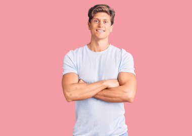 Sıradan kıyafetler giyen, kollarını kavuşturup kameraya bakan mutlu yüzlü genç bir adam. pozitif kişi. 