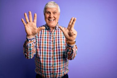 Üst düzey yakışıklı, parlak gömlekli, izole edilmiş mor arkaplanlı, kendine güvenen ve mutlu gülümseyen, sekiz numaralı parmaklarıyla işaret eden adam..