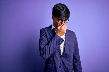 Ceket ve gözlük takan genç yakışıklı bir iş adamı. Mor arka planda izole edilmiş. Kokuşmuş ve iğrenç bir koku alıyor. Kötü kokuyor.