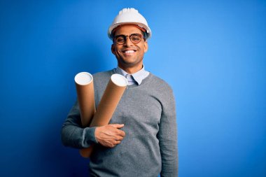 Genç Afro-Amerikan Afro-Amerikan mimar güvenlik kaskı takıyor elinde mutlu yüzlü planlar duruyor ve gülümsüyor dişlerini gösteren bir gülümsemeyle
