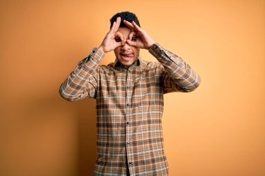 Sarı arka plan üzerinde duran sıradan tişörtlü genç yakışıklı bir adam. Dürbün gibi güzel hareketler yapıyor, gözleri parmaklarından bakıyor. Çılgın ifade.