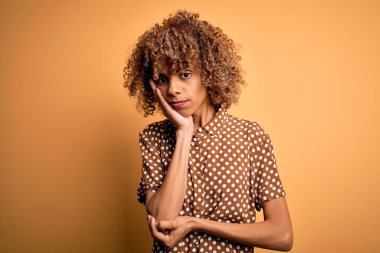 Genç, güzel, Afro-Amerikalı bir kadın sarı arka planda dikilmiş kollarını kavuşturup depresyondan sıkılmış ve yorgun görünüyor..