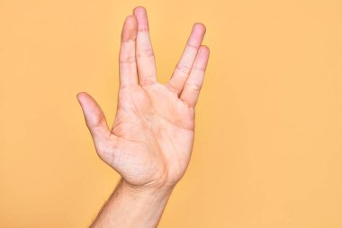 Kafkasyalı genç adam parmaklarını izole edilmiş sarı arka planda gösteriyor. Vulkan selamı veriyor, el ve parmaklarını gösteriyor, ucube kültürü sergiliyor.
