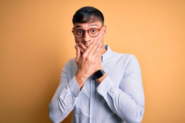 Sarı arka planda inek gözlüğü takan genç, yakışıklı İspanyol iş adamı yanlışlıkla ağızlarını kapatarak şok oldu. Gizli konsept.