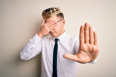 İzole edilmiş arka planda altın taç takan yakışıklı beyaz bir işadamı ellerle gözlerini kapatıyor ve hüzünlü ve korku dolu bir ifadeyle dur hareketi yapıyor. Utanç verici ve olumsuz bir kavram..