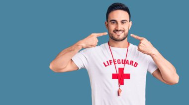 Cankurtaran üniforması giyen, neşeli gülümseyen, parmakları, dişleri ve ağzıyla işaret eden genç yakışıklı bir adam. diş sağlığı kavramı. 