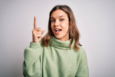 Kışlık süveter giyen genç, güzel sarışın kız izole arka planda dikiliyor ve başarılı bir fikri işaret ediyor. Heyecanlı ve mutlu. Bir numara..