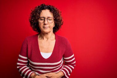 Orta yaşlı güzel kıvırcık saçlı kadın kırmızı arka planda sıradan çizgili kazak giyiyor hazımsızlık, acı verici hastalıklar yüzünden. Ache kavramı.