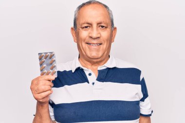 Elinde haplar olan yaşlı bir adam pozitif ve mutlu görünüyor. Kendine güvenen bir gülümsemeyle ayakta duruyor ve dişlerini gösteriyor. 