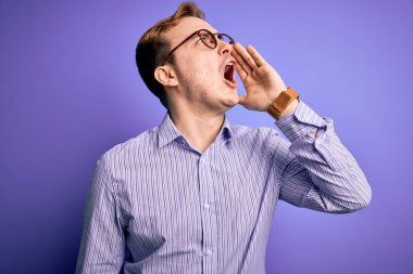 Genç ve yakışıklı kızıl saçlı bir adam mor arka planda günlük gömlek ve gözlük takıyor ve avazı çıktığı kadar bağırıyor. İletişim konsepti.