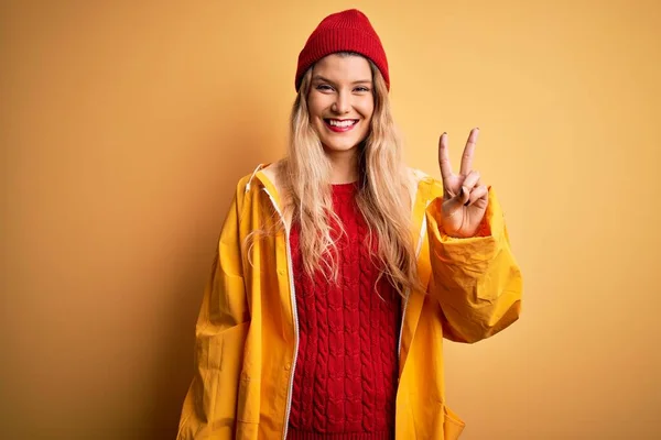 Young Beautiful Blonde Woman Wearing Raincoat Wool Cap Isolated Yellow — Stock Photo, Image