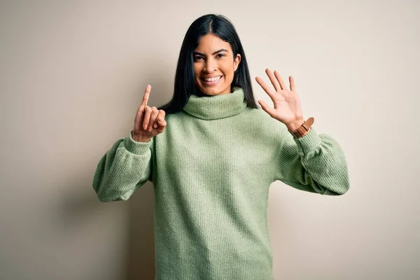 Young beautiful hispanic woman wearing green winter sweater over isolated background showing and pointing up with fingers number six while smiling confident and happy.