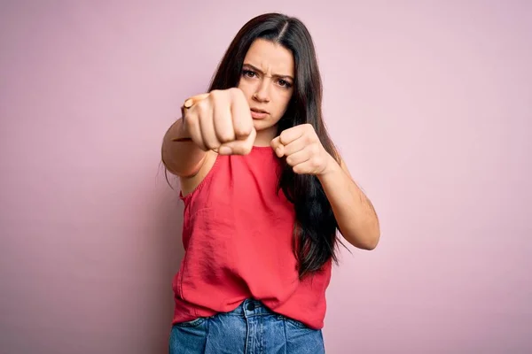 Young brunette woman wearing casual summer shirt over pink isolated background Punching fist to fight, aggressive and angry attack, threat and violence