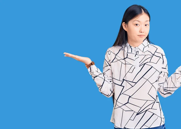 若い美しい中国の女性は カジュアルなシャツを着て腕や手で混乱した表現を調達しました 疑わしい概念 — ストック写真