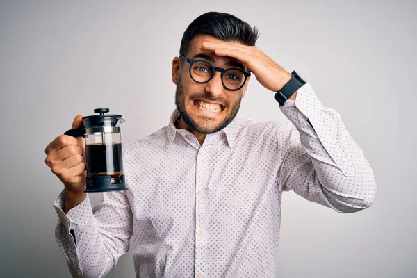 Young handsome man making coffee using french press coffeemaker over isolated background stressed with hand on head, shocked with shame and surprise face, angry and frustrated. Fear and upset for mistake.