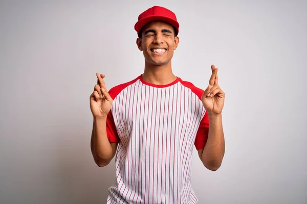 縞模様の野球Tシャツとキャップジェスチャーの指を身に着けている若いハンサムなアフリカ系アメリカ人スポーツマンは希望と目を閉じて笑顔を交わした 幸運と迷信の概念 — ストック写真