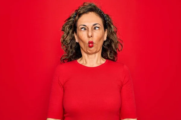 中年老年黑发女人穿着休闲T恤 站在红色背景之上 用嘴唇 疯狂和滑稽的姿势做鱼脸 有趣的表达方式 — 图库照片