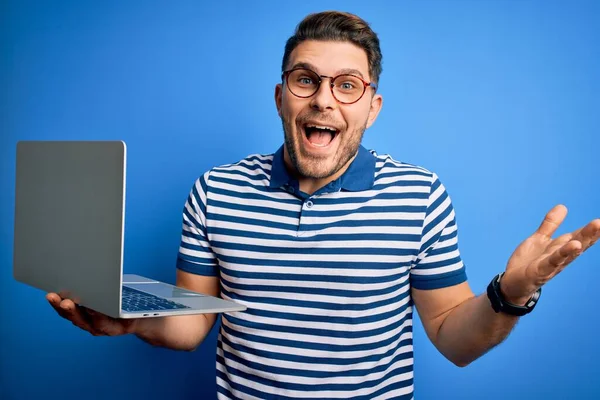 コンピューターのノートパソコンで働く青い目をした青い目の若いビジネスマンはとても幸せで興奮し 大きな笑顔で叫んで勝利を祝う勝者の表現と手を上げ — ストック写真