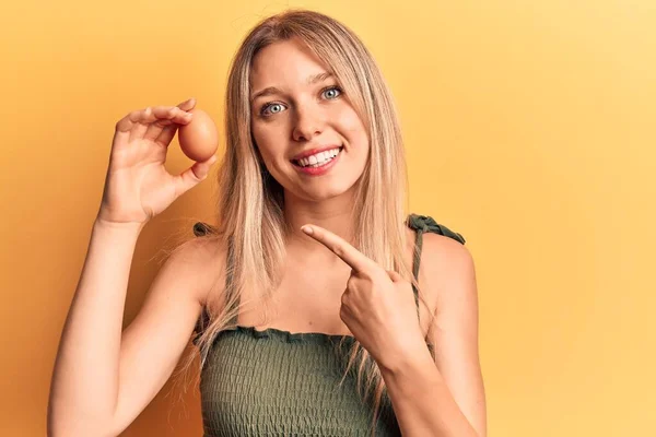 Young Blonde Woman Holding Egg Smiling Happy Pointing Hand Finger — ストック写真