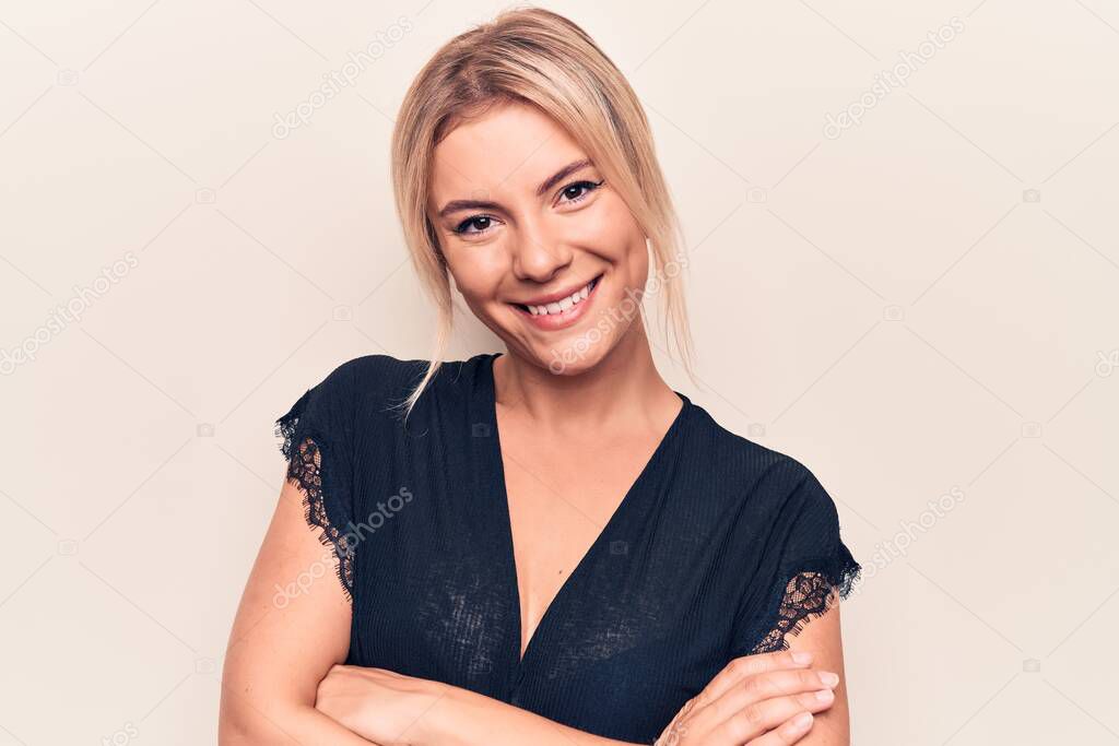 Young beautiful blonde woman wearing casual t-shirt standing over isolated white background happy face smiling with crossed arms looking at the camera. Positive person.