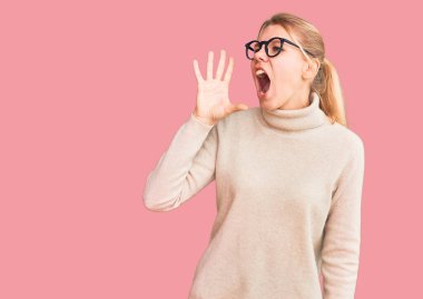 Balıkçı yaka kazak giyen, gözlüklü genç ve güzel bir kadın bağırıyor ve ağızdan ağıza bağırıyor. iletişim konsepti. 