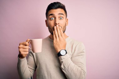 Genç yakışıklı adam pembe izole edilmiş arka planda bir fincan sıcak kahve içiyor. Ağzı kapalı, utancından ağzı açık kalmış, korkunun dışa vurumu, sessizlikten korkması, gizli konsept.